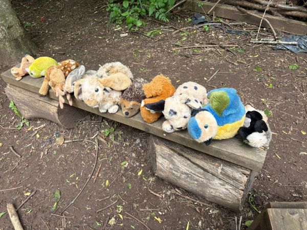 Stuffed animals lined up on a rustic outdoor wooden bench.