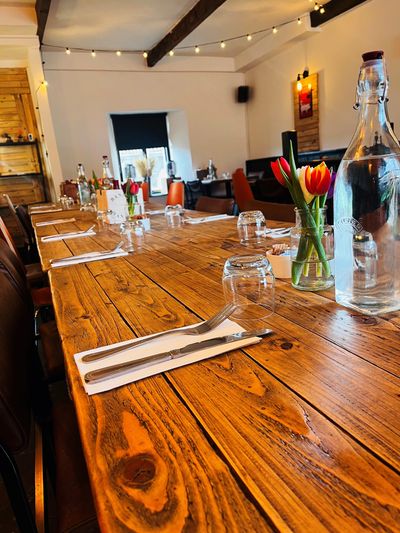 Cozy wooden dining table set with flowers, glasses, and cutlery in a warmly lit room.