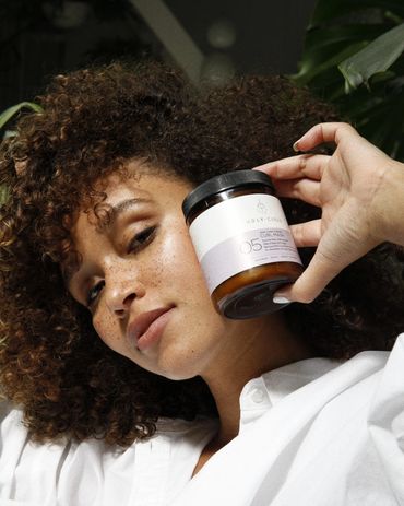Woman with curly hair holding a jar of curl mask near her face.