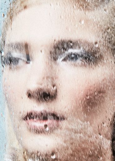 Close-up of a woman's face through a water-covered glass.