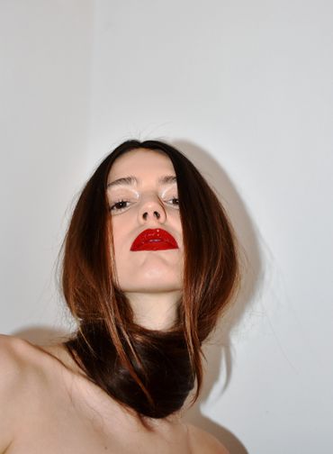 Low-angle portrait of a woman with bold red lips and long brown hair wrapped around her neck.