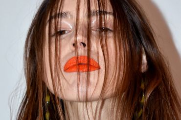 Close-up of a woman with striking orange lipstick and hair partially covering her face.
