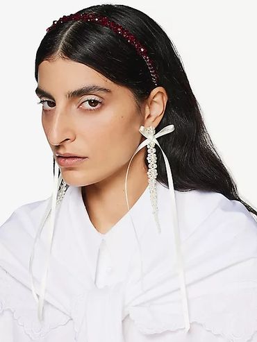 Woman with long dark hair wearing pearl drop earrings and a beaded headband.
