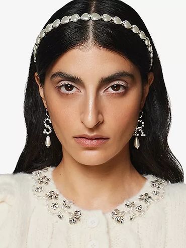 Woman with pearl headband, pearl earrings, and embellished white top.