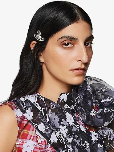 Woman with long dark hair wearing a floral scarf and a plaid top, accessorized with a silver hair clip.