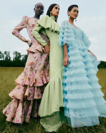 Three models in elegant, textured gowns posing outdoors in a grassy field.
