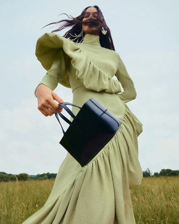 Woman in a flowing green dress holding a black handbag in a field.