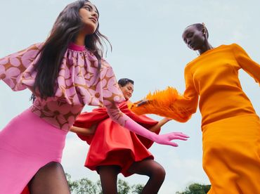 Three women in vibrant, colorful dresses posing dynamically against the sky.