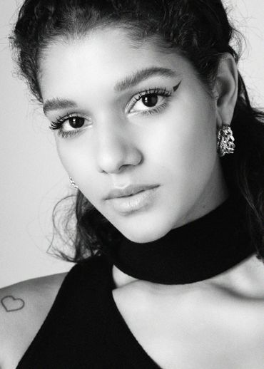 Black and white close-up portrait of a woman with eyeliner and a heart tattoo.