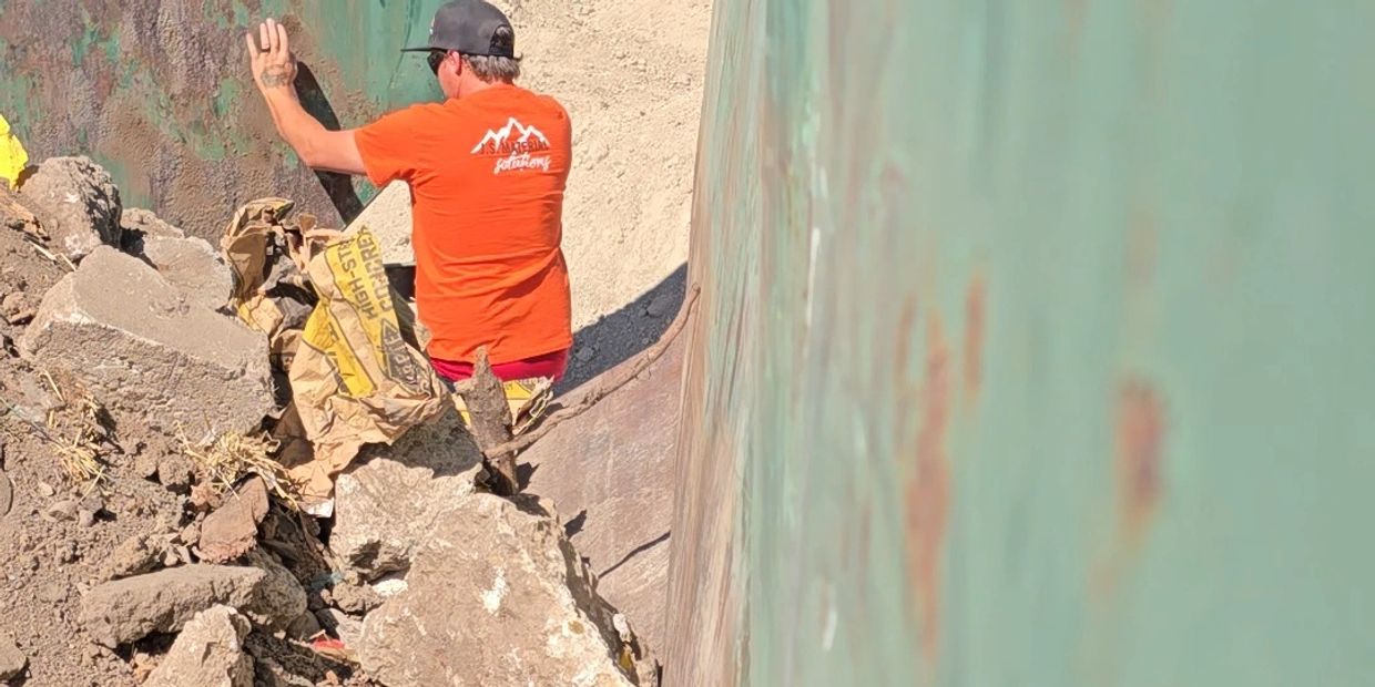 A person in an orange shirt working amidst debris and rocks at a construction site.