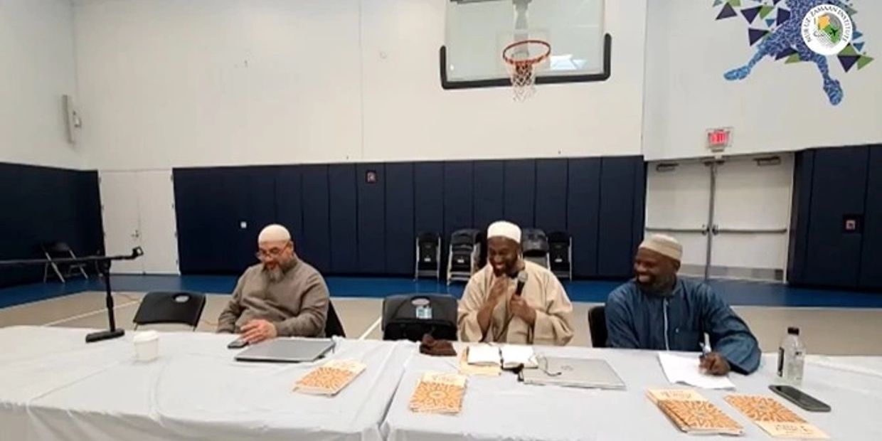 Three men sitting at a table in a gymnasium, engaged in discussion.