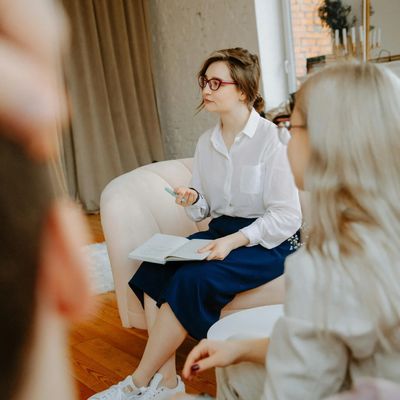 A woman in glasses holding a notebook and pen while engaged in a group discussion.