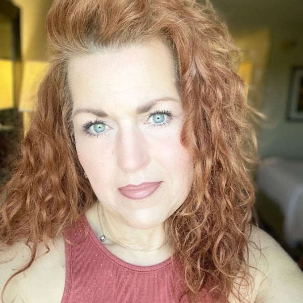 Close-up of a woman with curly red hair and blue eyes.