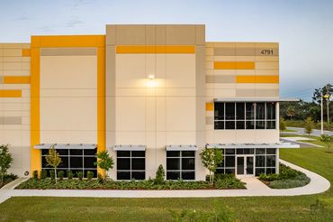 Modern beige and yellow commercial building with large windows and landscaped greenery.