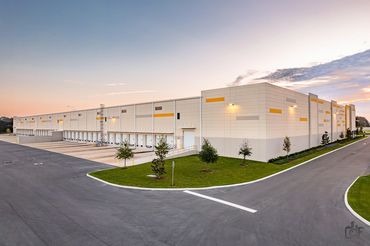 Modern warehouse building with multiple loading docks and a spacious driveway at sunset.
