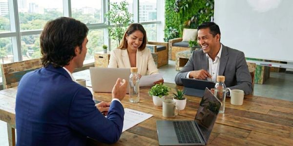 Three professionals engaged in a lively business meeting at a wooden table.