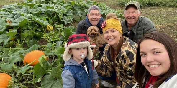 A family enjoys a pumpkin patch outing with their dog on a cloudy day.