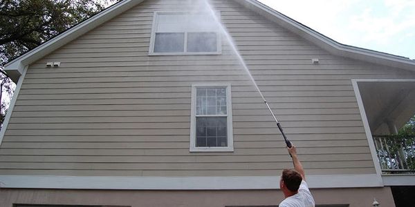 Man power washing the upper wall of a house with a long wand.