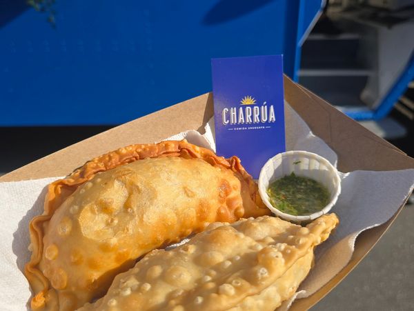 Two golden empanadas with green sauce from Charrúa food truck.