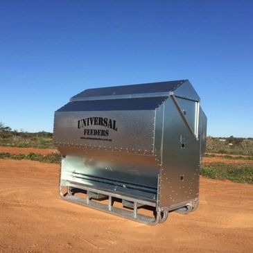 Large metal livestock feeder labeled Universal Feeders on dirt ground.