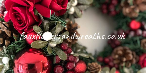Festive wreath adorned with red roses, berries, pine cones, and a shiny red ornament.