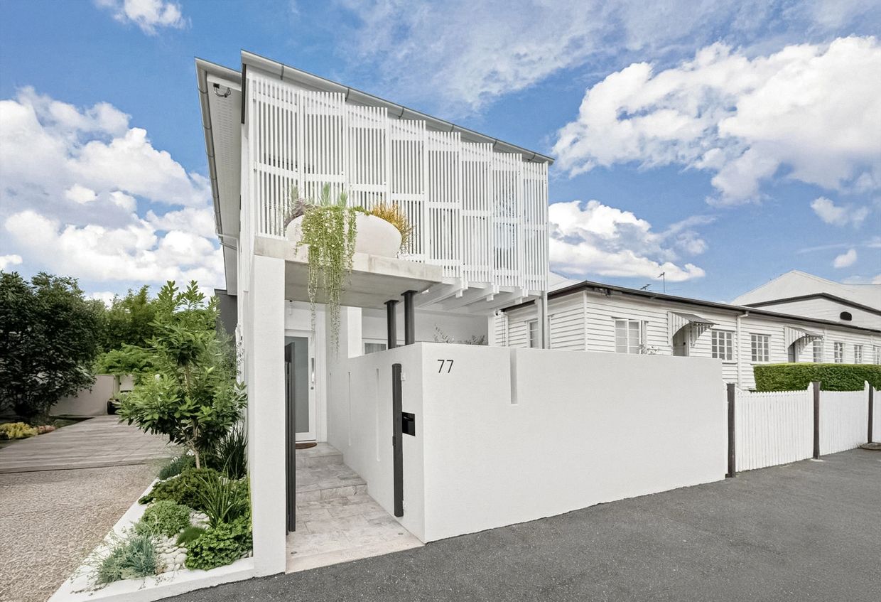 Modern white house with vertical slatted design and lush greenery.