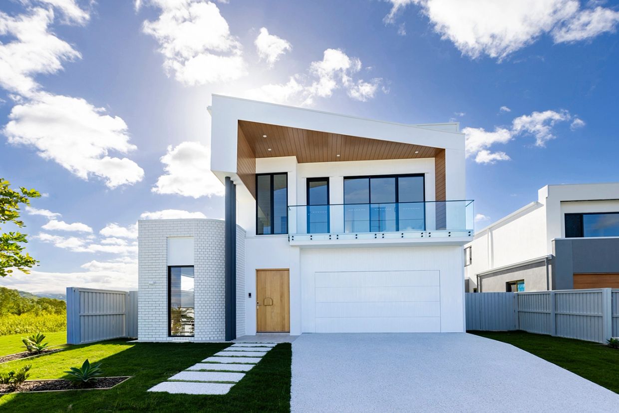 Modern two-story white house with a wooden door and glass balcony under a blue sky.