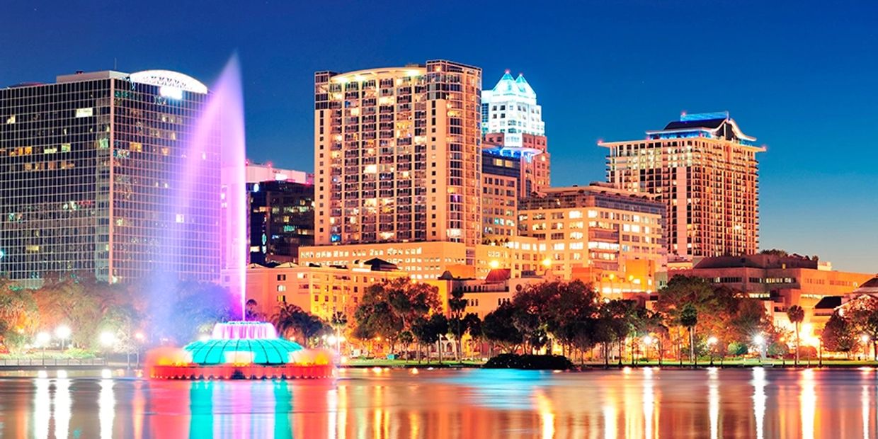 City skyline at night with a colorful illuminated fountain reflecting on the water.