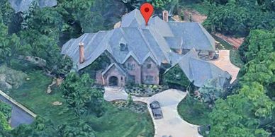 A large house with a gray roof surrounded by greenery and a driveway.