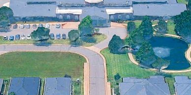 Aerial view of a residential area with houses, a pond, and parked cars.