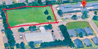 Aerial view of a green field marked with a red boundary in a residential area.