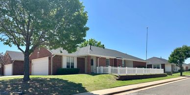 Single-story brick house with a white porch and garage under a clear blue sky.