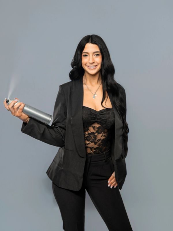Woman spraying hairspray, dressed in black attire.
