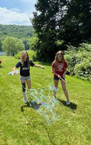 Two girls outdoors making a giant soap bubble on a sunny day.