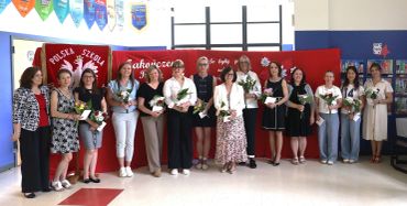 A group of women holding flowers posing indoors in front of a red backdrop.