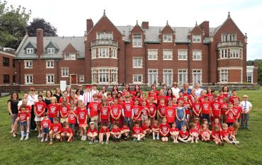 Large group of children and adults in red shirts posing in front of a historical building.