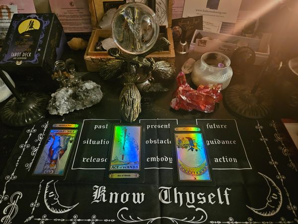 Tarot reading setup with cards, crystals, and a crystal ball on a cloth saying 'Know Thyself.'