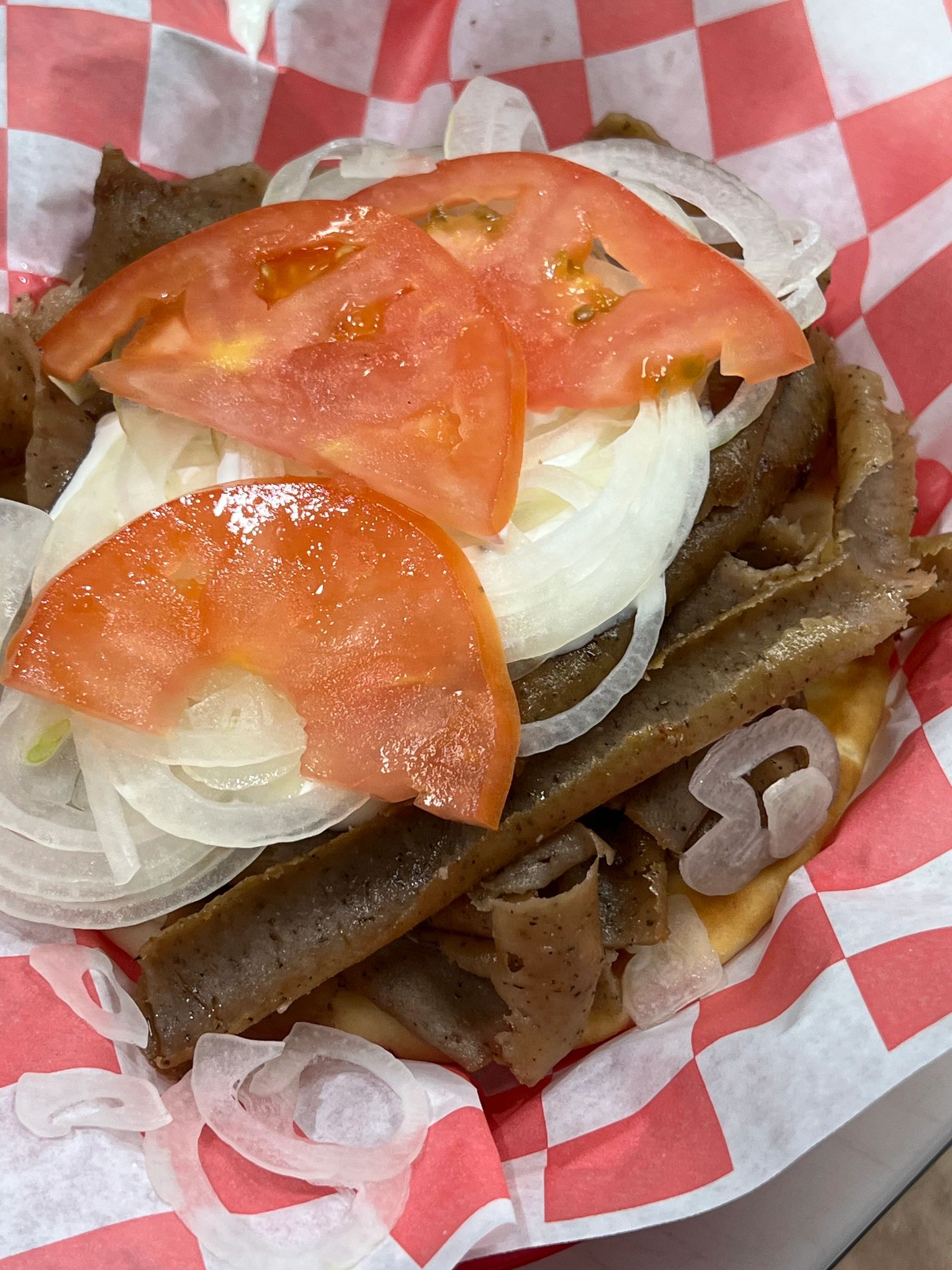 Gyro sandwich with sliced tomatoes and onions on a checkered paper.