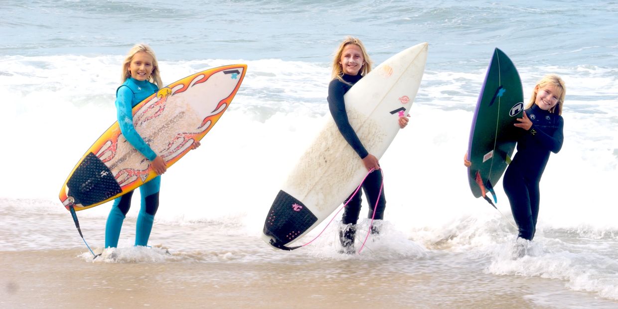 Three girls holding surfboards at the beach.