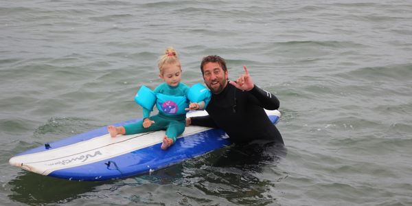 Man with a child on a surfboard in the ocean.