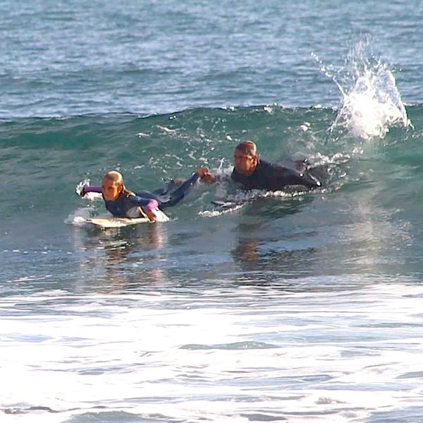 Two people surfing, one holding the other's hand.