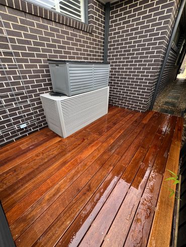 Wet wooden deck with brick walls and air conditioning units.