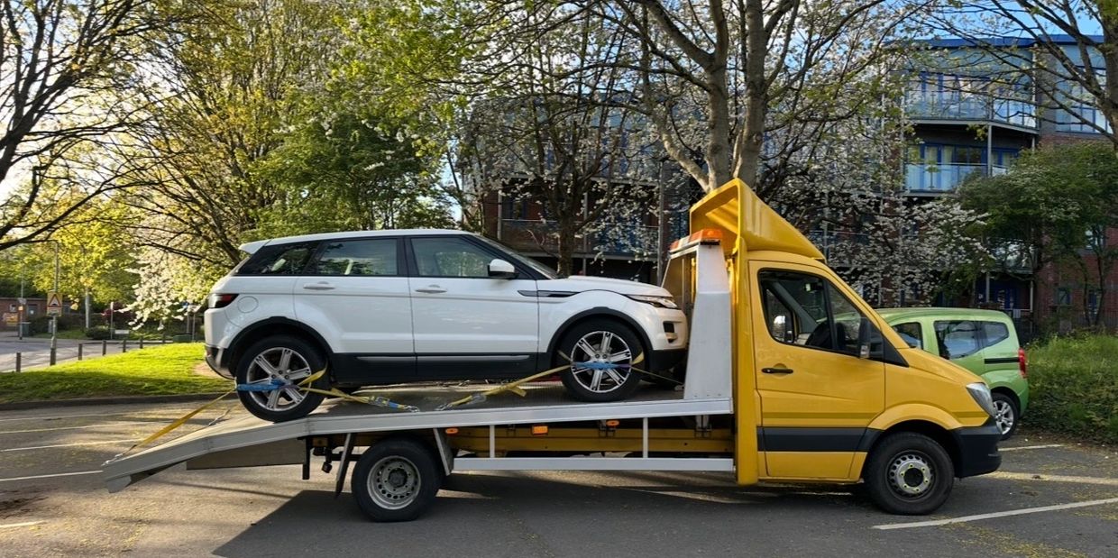 A white SUV secured on a yellow tow truck in a parking lot.