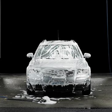 Car covered in foam during a wash in a dark setting.