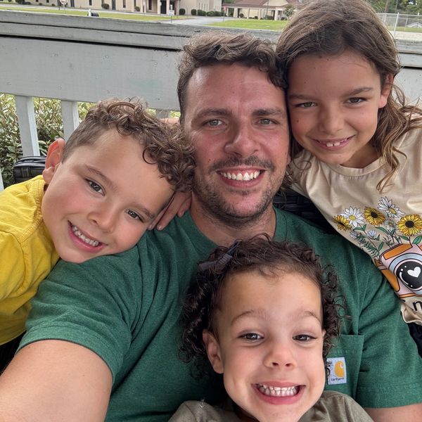 A happy man with three smiling children outdoors.