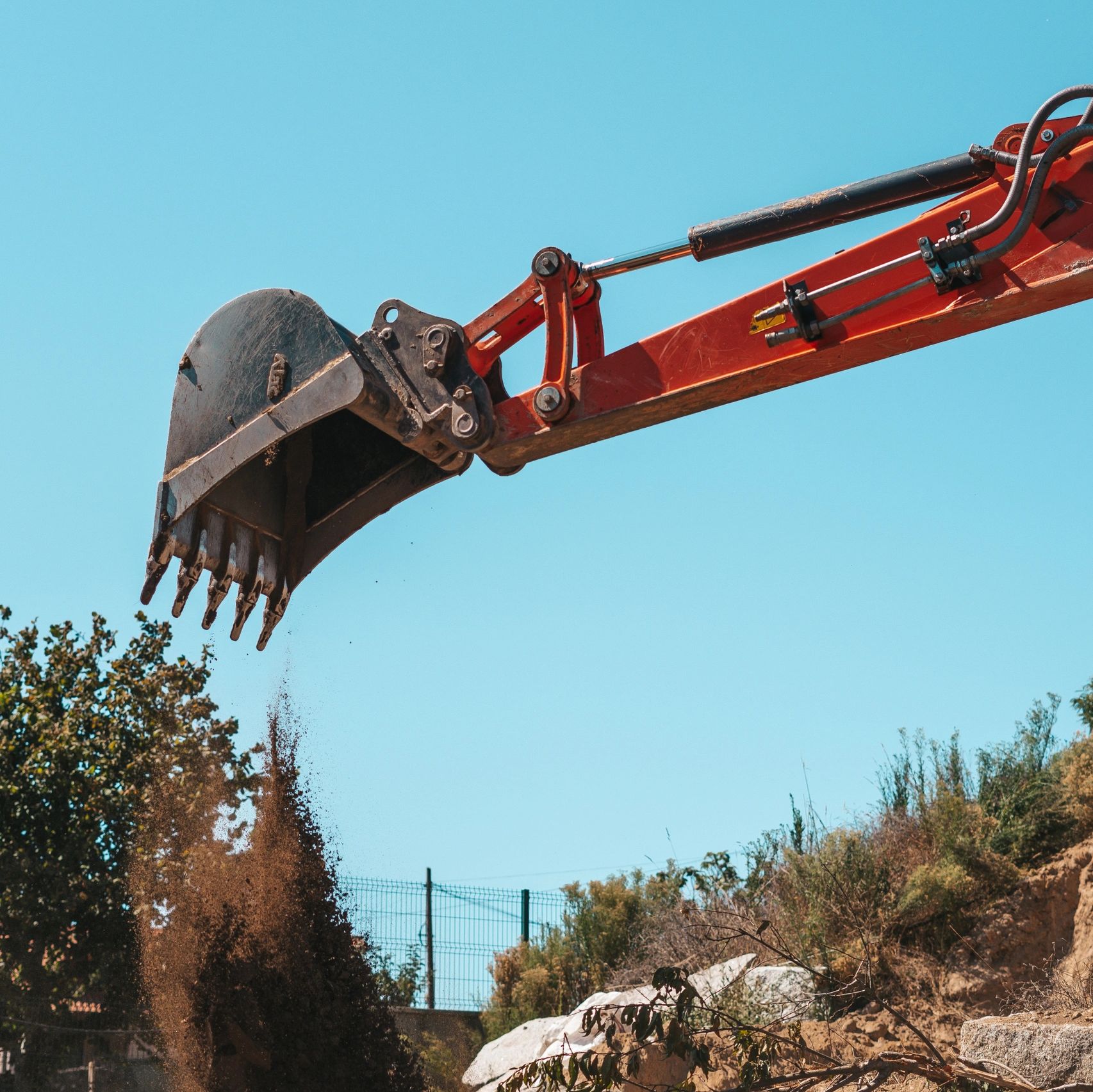 Excavator bucket dumping soil at a construction site on a clear day.