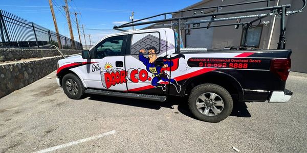A branded pickup truck for a door company with colorful graphics and contact info.