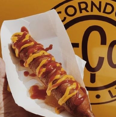 A corn dog drizzled with mustard and ketchup in a paper tray.