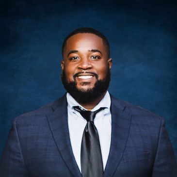 Smiling man in a suit and tie against a blue backdrop.