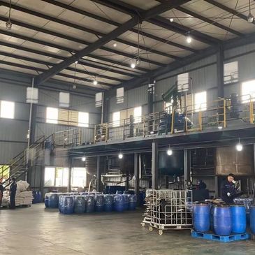 Inside a spacious industrial facility with workers and blue barrels.